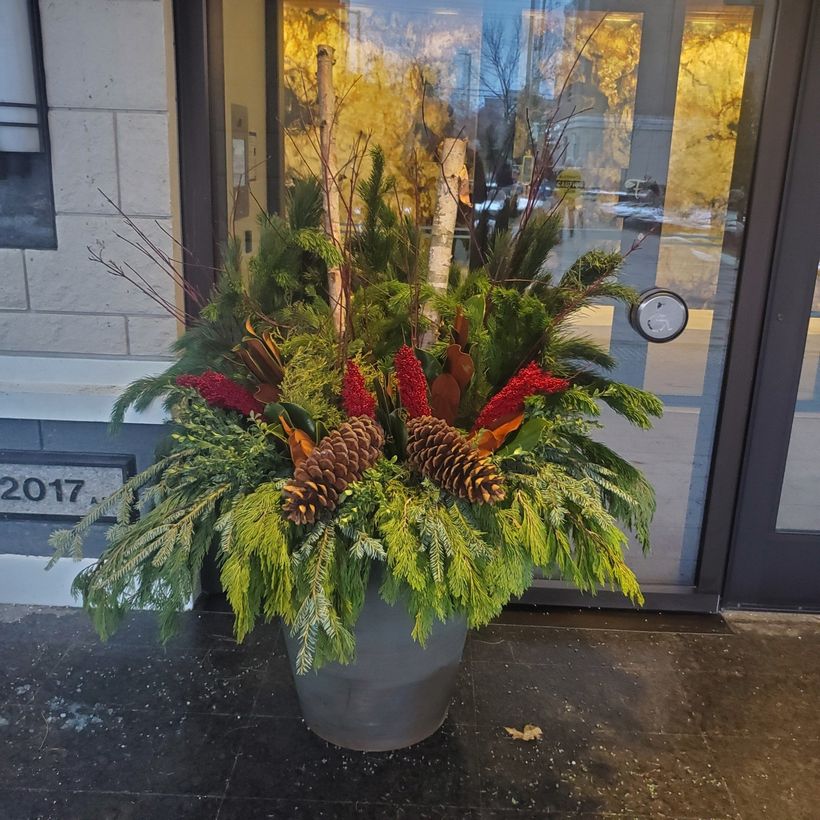 A planter with flowers and pine cones in front of a door that says 2017