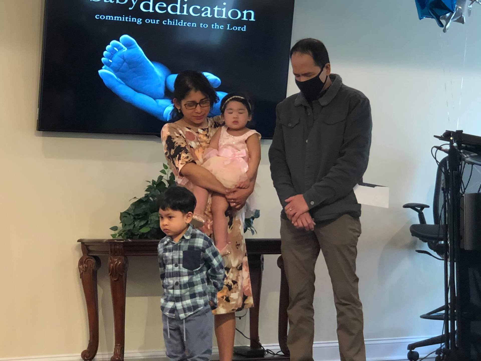Family of four posing on a stage with a blue event banner and a camera tripod nearby