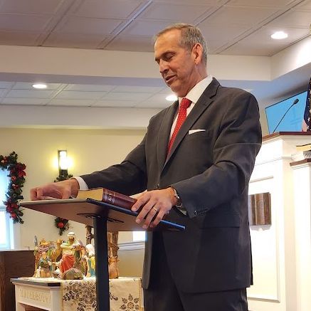 Man in a dark suit and red tie speaking at a lectern in a church-like room
