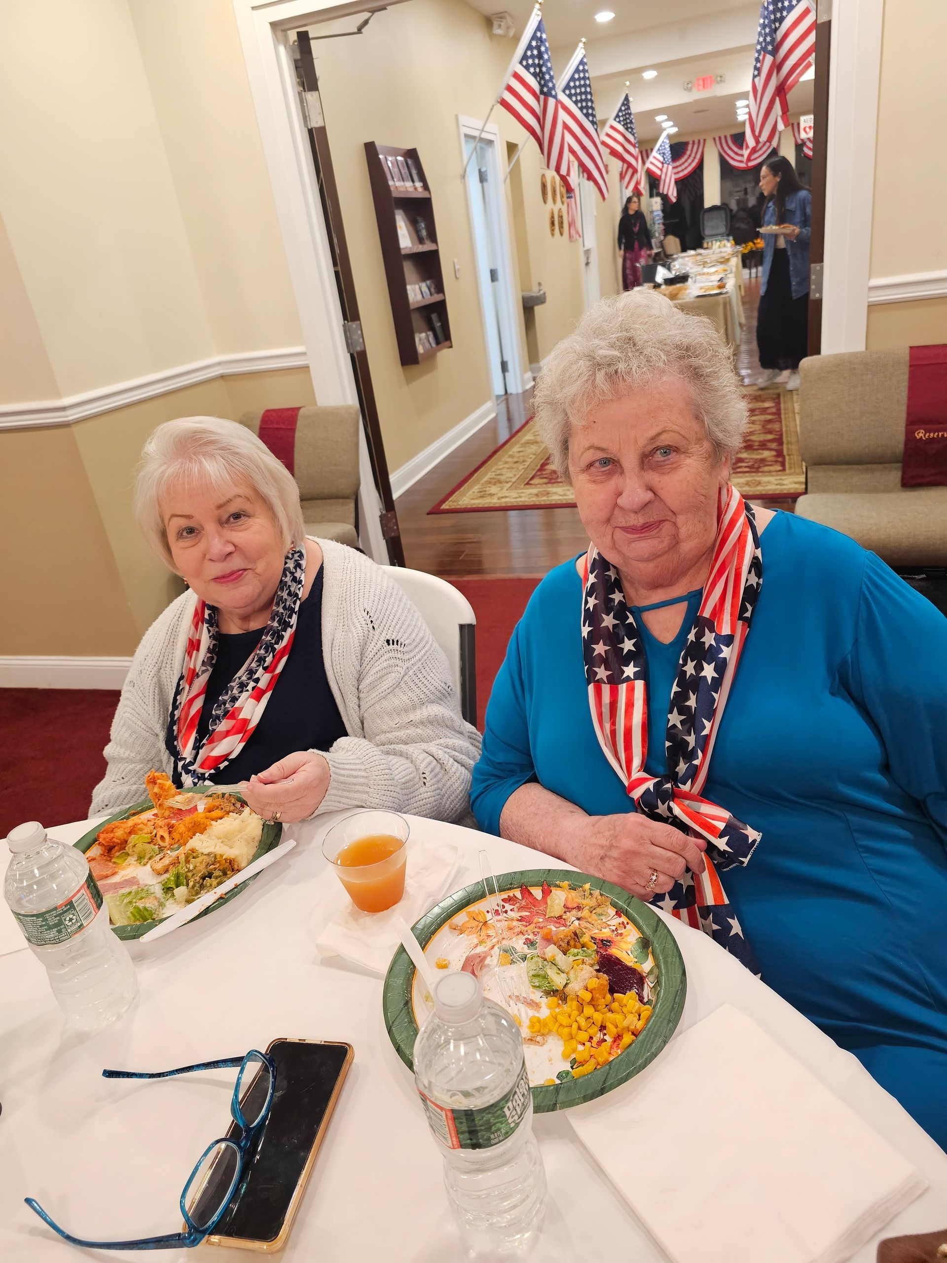 Two women seated at a table in a decorated dining hall, eating salad and drinks nearby.
