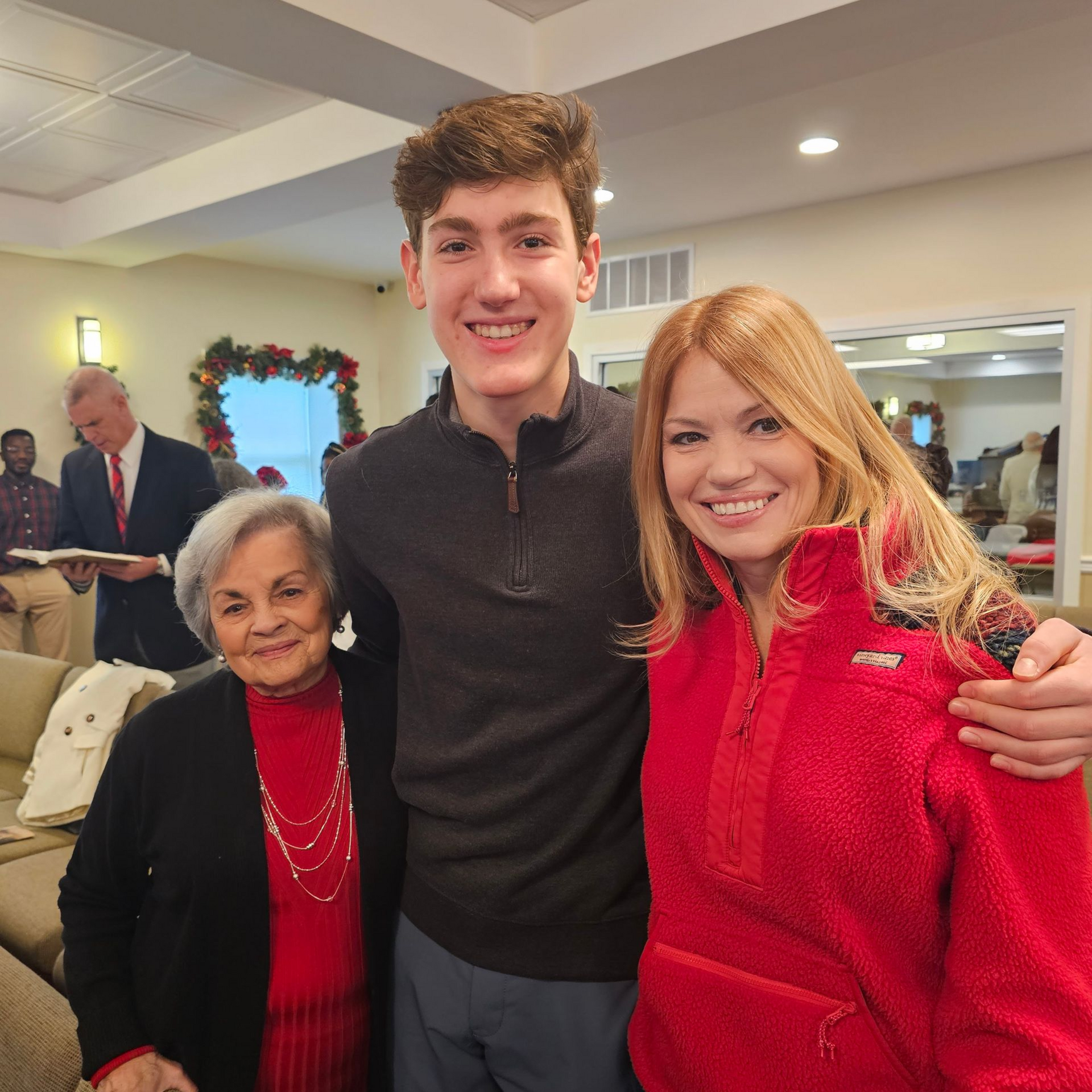 Three smiling people posing indoors, with two in red and black sweaters and one in a dark top.