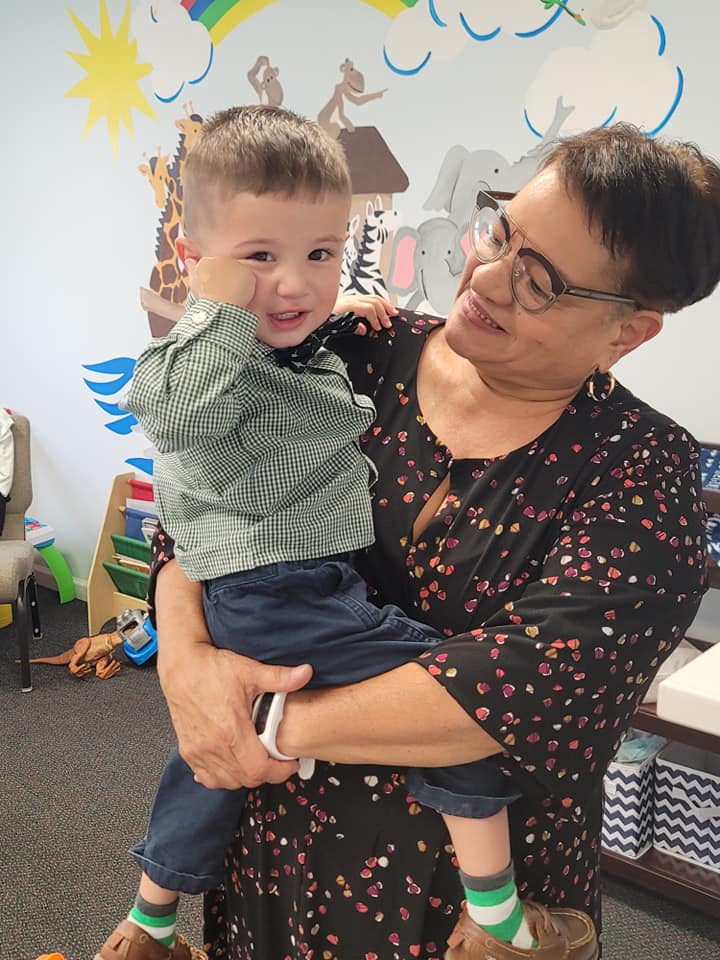 Adult holding smiling child indoors in a colorful classroom with painted wall art.