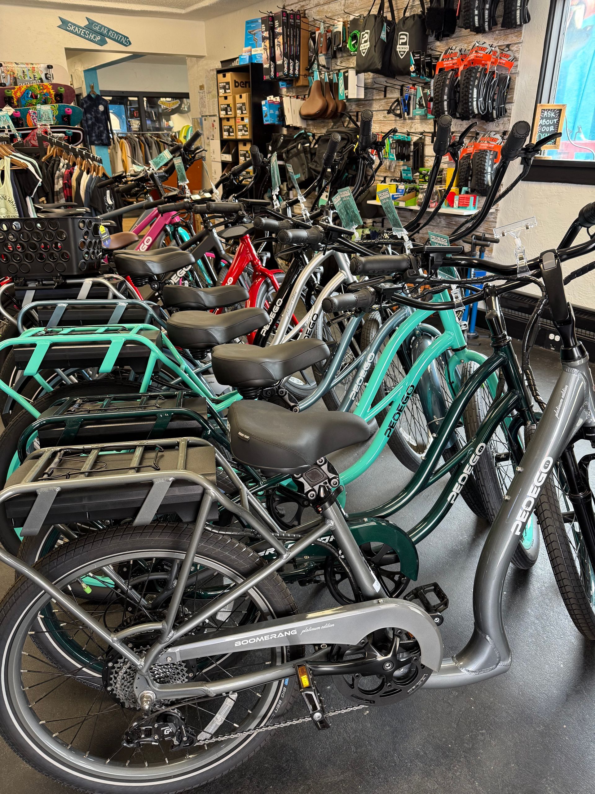 A row of bicycles, including teal and grey models, parked inside a bicycle shop with accessories displayed on the walls.