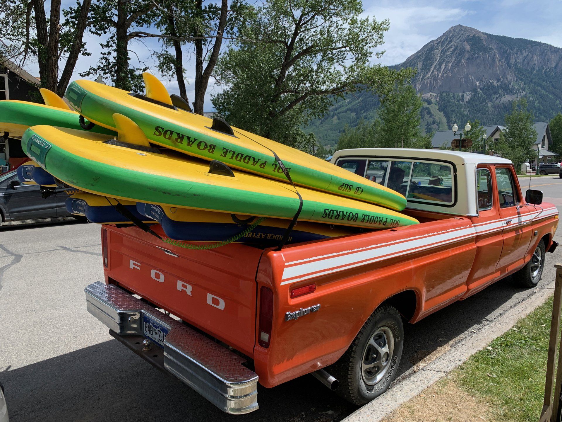 Orange pickup truck with yellow-green surfboards parked by a mountain road