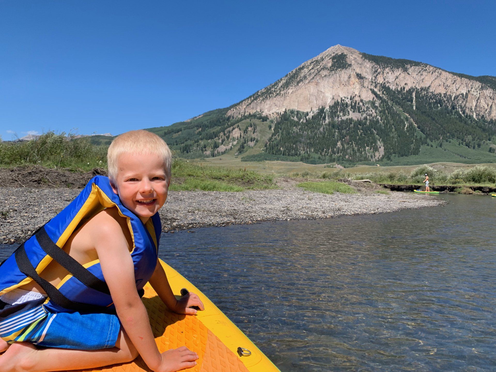 Smiling child in a yellow kayak on a river with mountains in the background