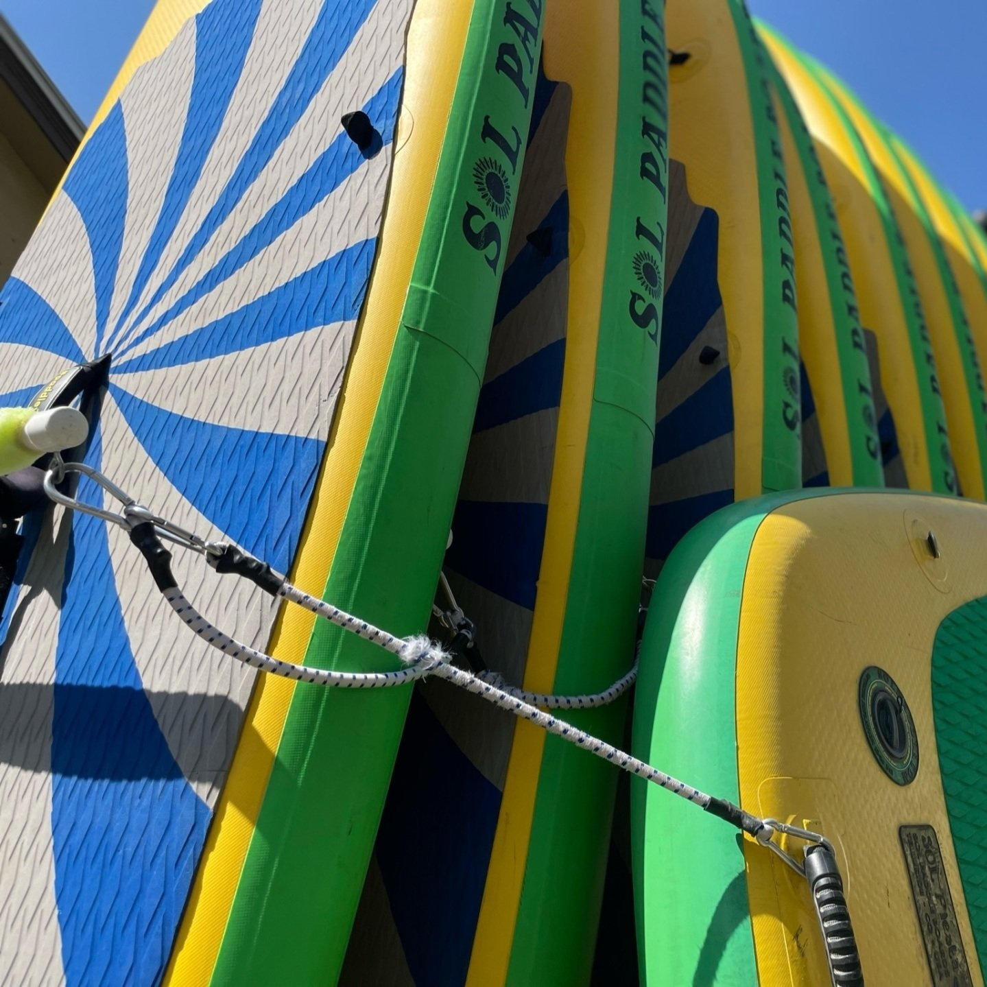 Close-up of colorful surfboards stacked together, with green, yellow, and blue stripes and a rope tie.