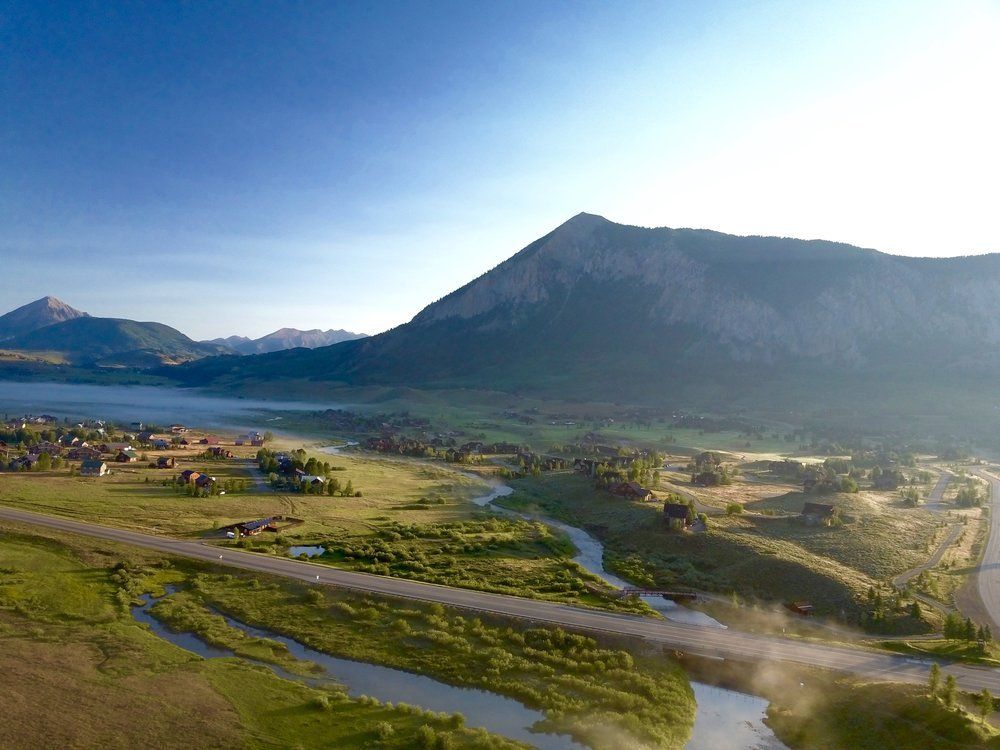 Mountain valley landscape with a winding river, green fields, and mist under a blue sky