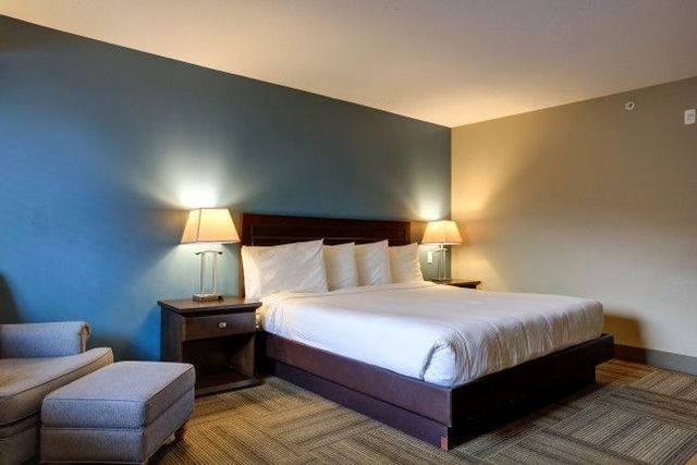 Hotel bedroom with king bed, two lamps, blue and beige walls, and a chair.
