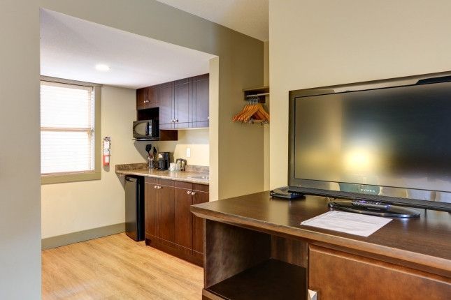 Hotel room with small kitchenette. Dark wood cabinets, microwave, mini-fridge. TV on desk.