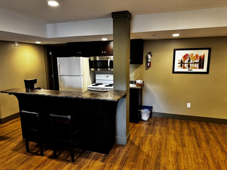 Kitchenette with dark cabinets, a breakfast bar, white appliances, and wooden flooring.