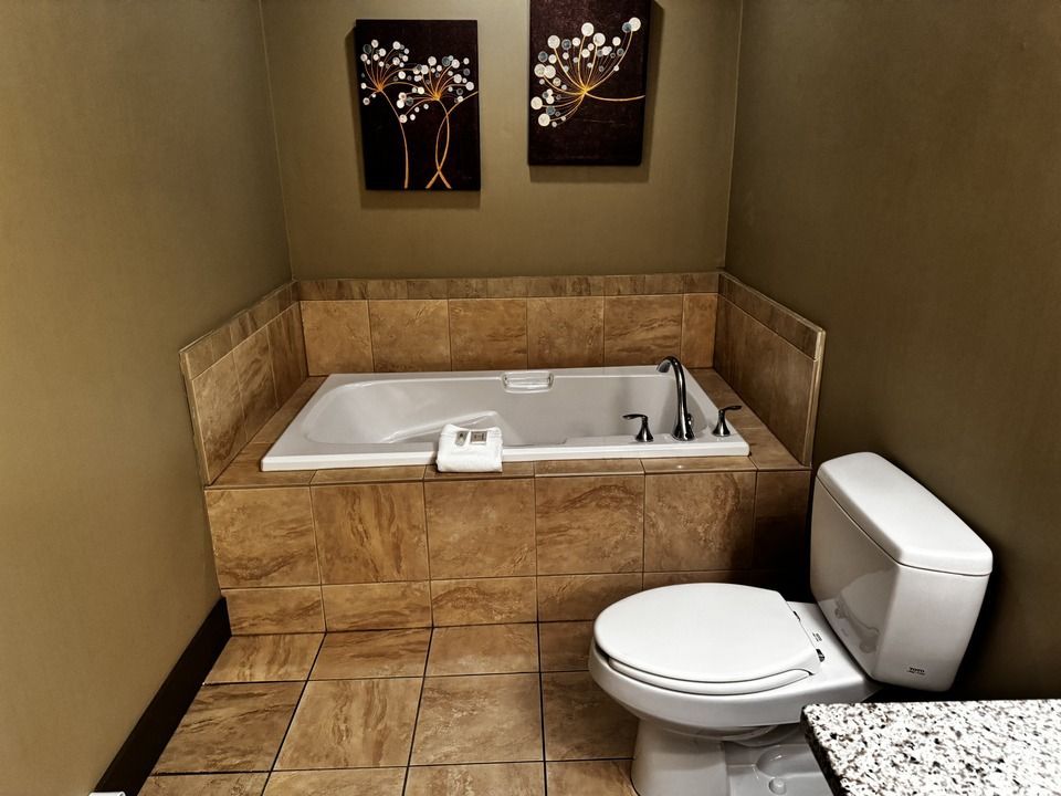 Bathroom with a built-in soaker tub and a toilet. The walls are neutral-colored with brown tile accents. 