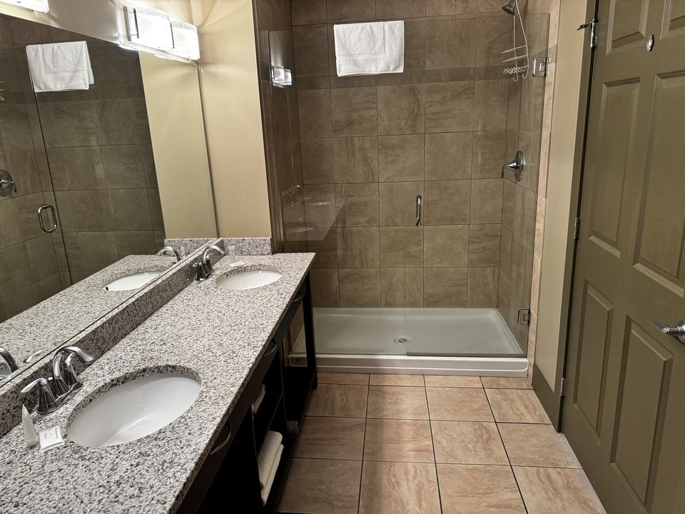 Bathroom with double sinks, walk-in shower, and tile floors.