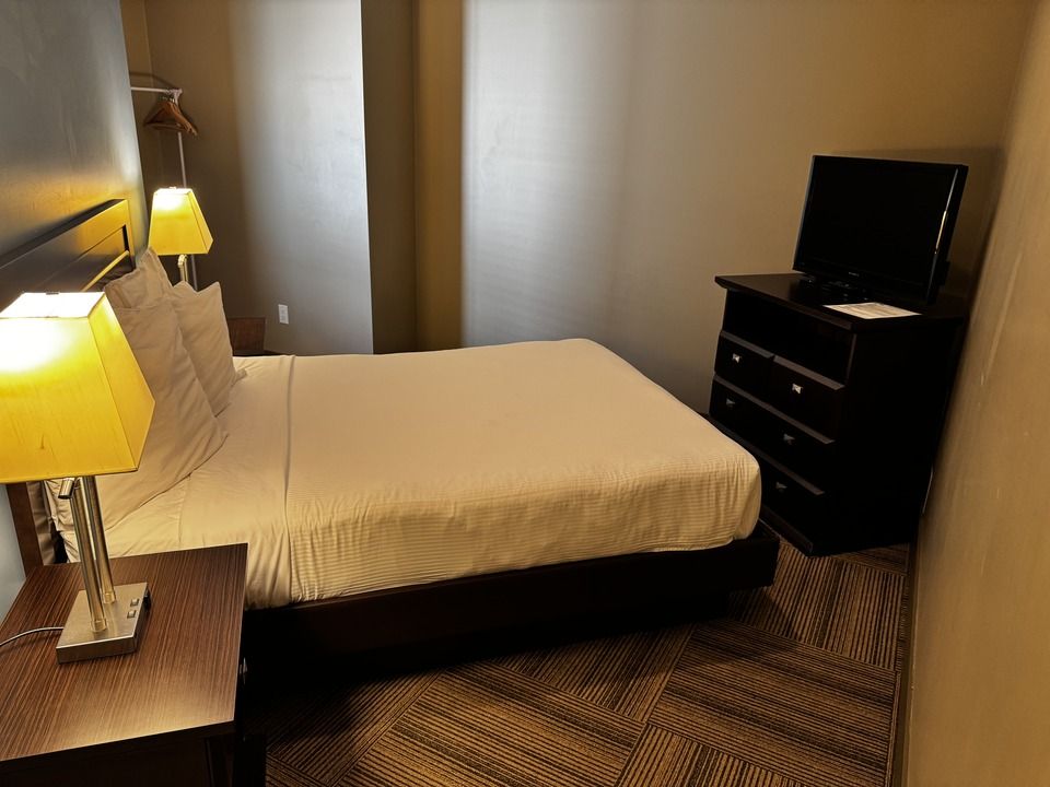 Bedroom with bed, nightstands, lamps, dresser with TV, and patterned carpet.