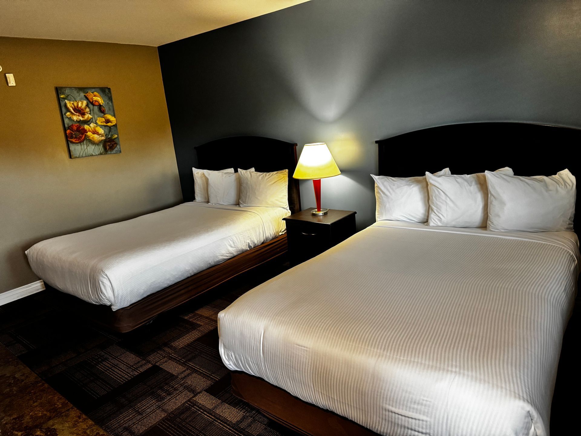Hotel room with two beds, lamp, and art on the wall.