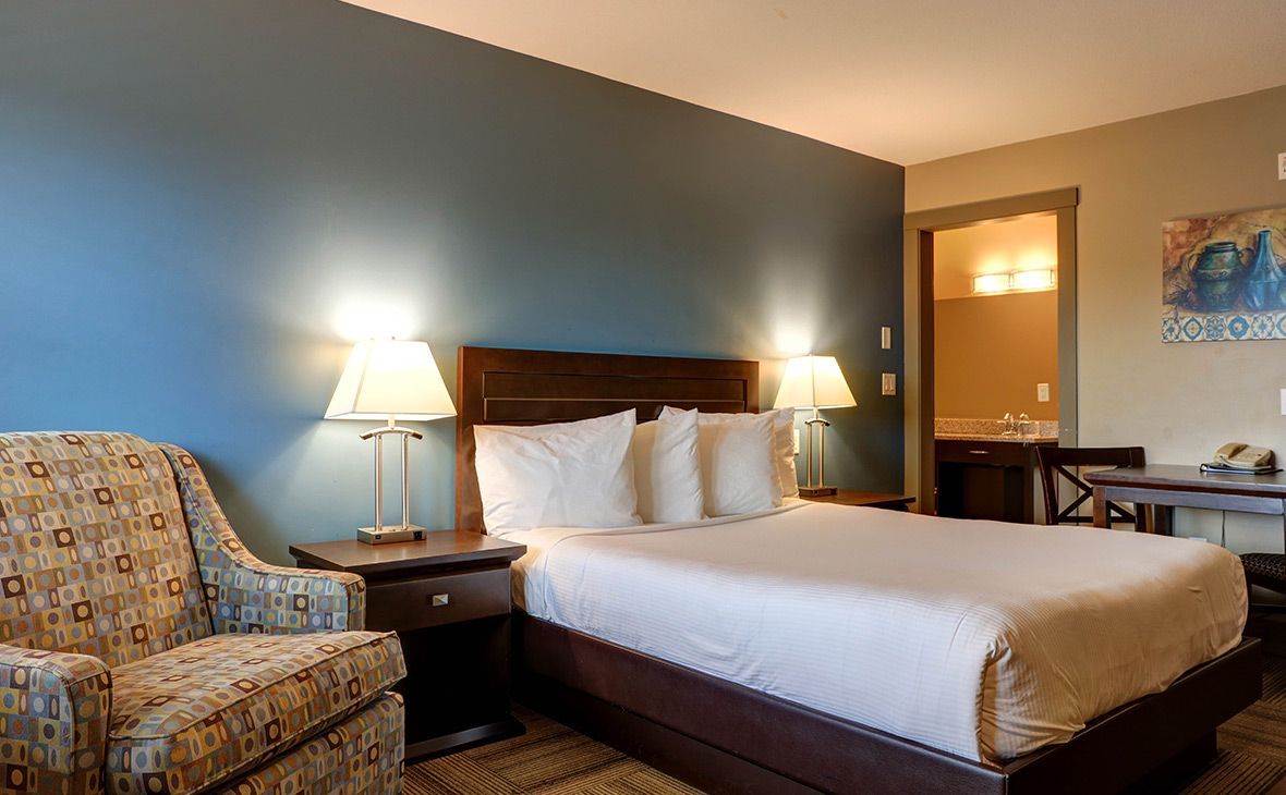 Hotel room with a bed, armchair, nightstands, and a bathroom visible. Blue wall.