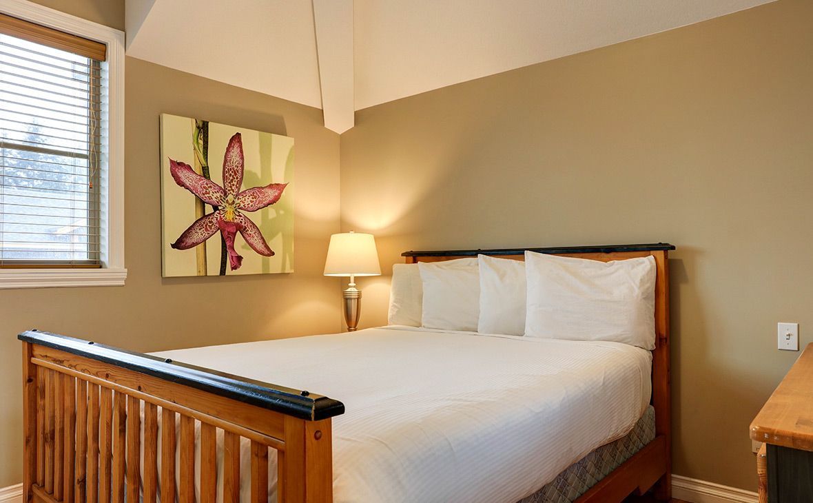 Bedroom with wooden bed frame, white bedding, and artwork of a flower; beige walls.
