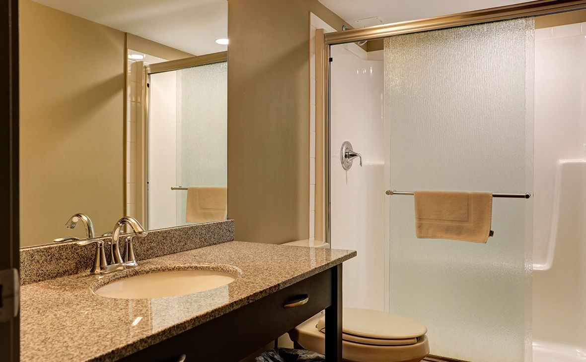Bathroom with granite countertop, sink, shower, and toilet. Beige walls and a mirror.