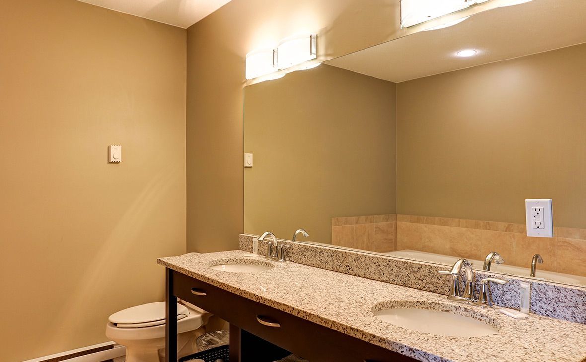 Bathroom with double sinks, large mirror, granite countertop, beige walls, and overhead lighting.