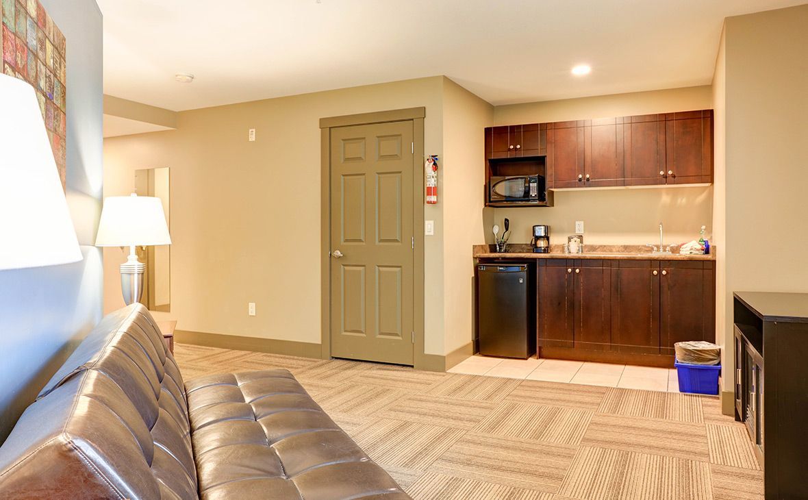A hotel room with a kitchenette featuring a mini-fridge, microwave, and cabinetry.