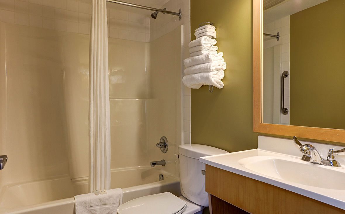 Bathroom with shower, toilet, sink, and towels. Cream-colored walls and green accent wall.