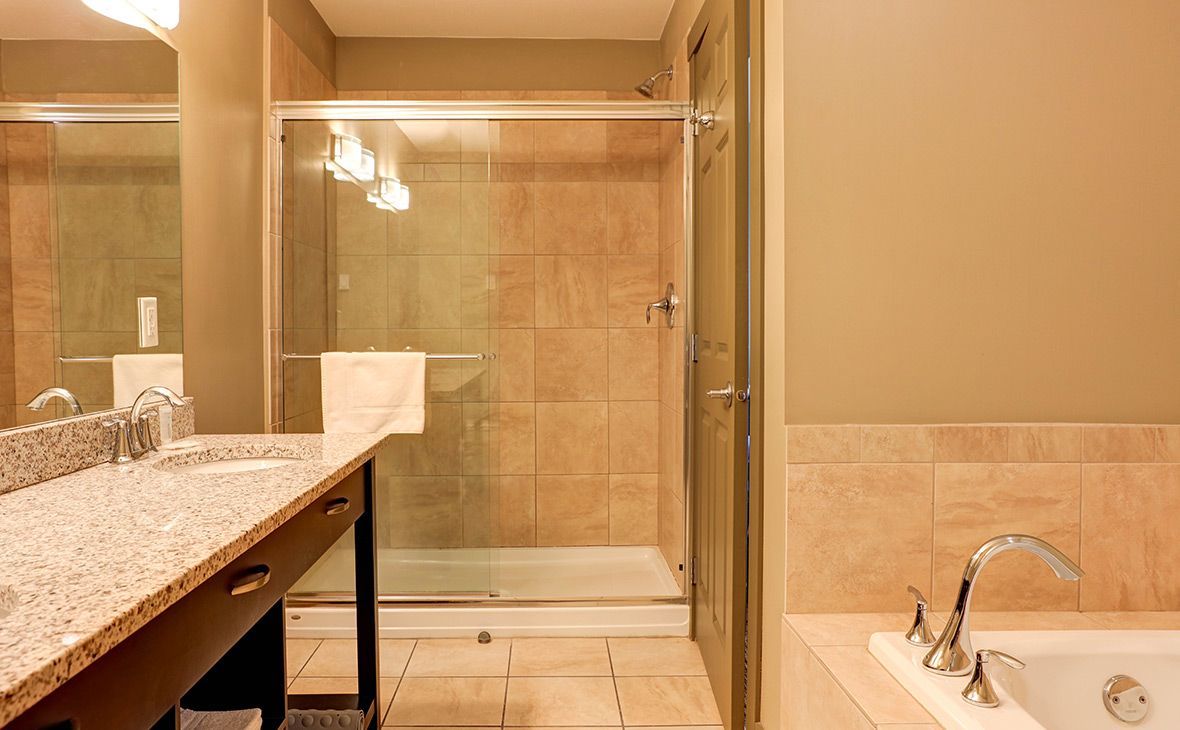 Bathroom with beige tiled shower, tub, and vanity with granite countertop.