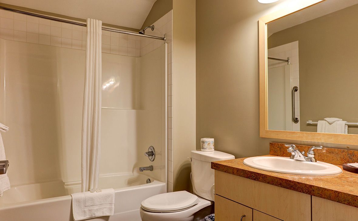 Bathroom with white bathtub, toilet, sink, and mirror. Tan walls, beige countertop.