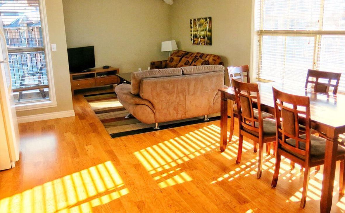 Bright living and dining area with wood floors, table with chairs, and two sofas.