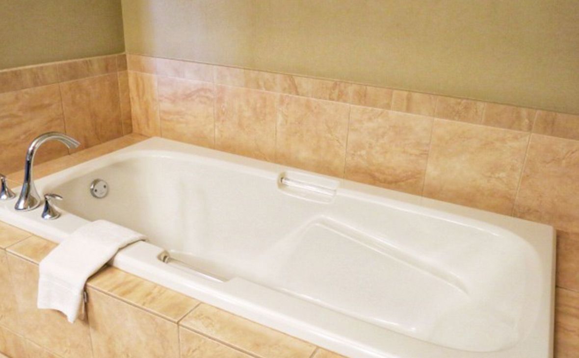 White bathtub in a tile-lined alcove; towel on side. Chrome faucet, tan walls.