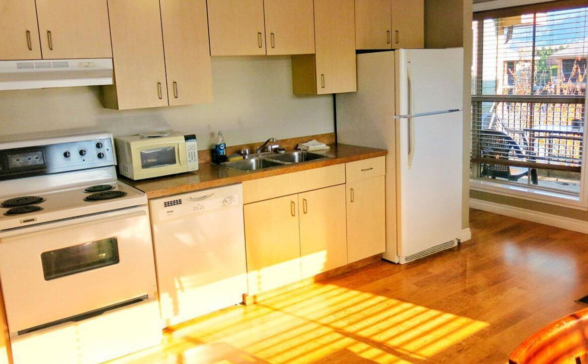 Kitchen with light wood cabinets, white appliances, and a window to a balcony.