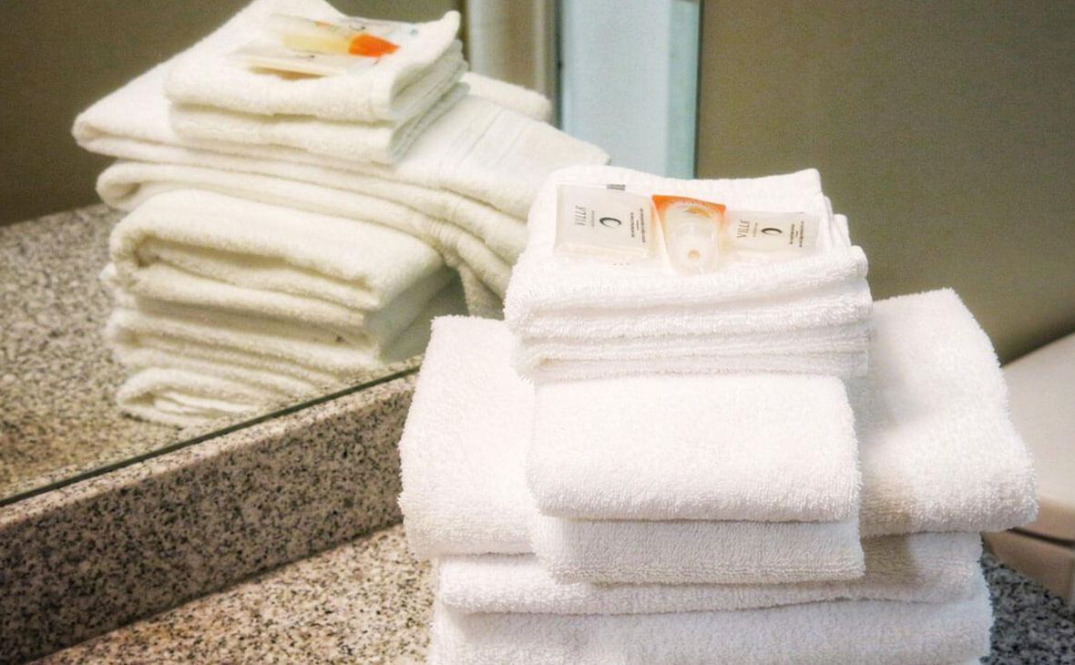 White folded towels with toiletries in a bathroom, reflected in a mirror.