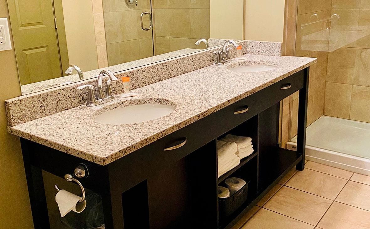 Bathroom with double sink vanity, granite countertop, black cabinets, and towels. Shower visible.