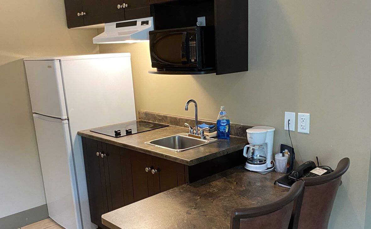 Small kitchenette with fridge, microwave, sink, stovetop, coffee maker, and seating.