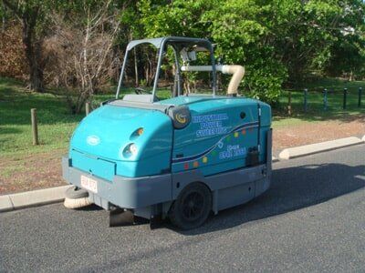 Blue street sweeper on asphalt road, parked next to curb and trees — Industrial Power Sweeping Services Pty Ltd In Knuckey Lagoon, NT