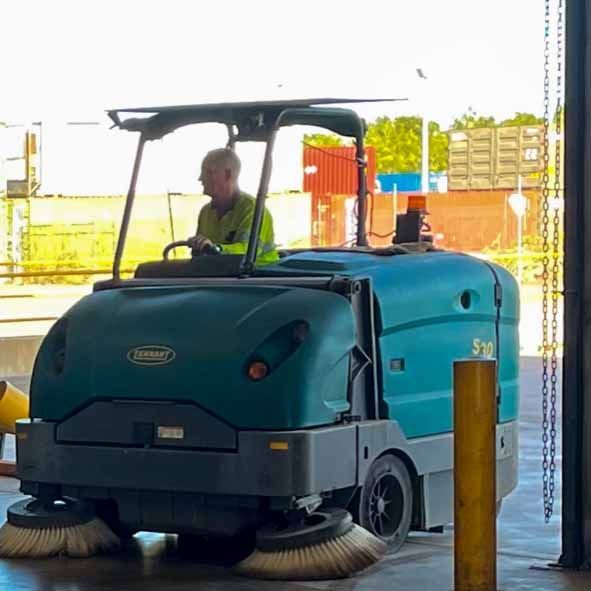 A person operating a teal industrial sweeper. The sweeper has two front brushes. Warehouse setting — Industrial Power Sweeping Services Pty Ltd In Knuckey Lagoon, NT