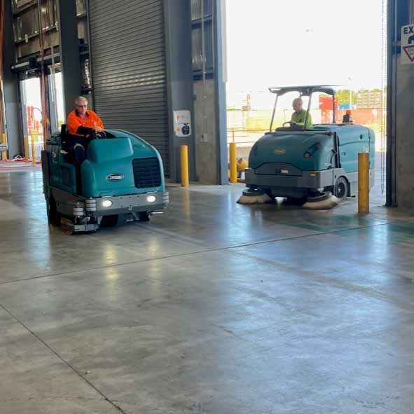 Two teal industrial floor sweepers cleaning a warehouse — Industrial Power Sweeping Services Pty Ltd In Knuckey Lagoon, NT