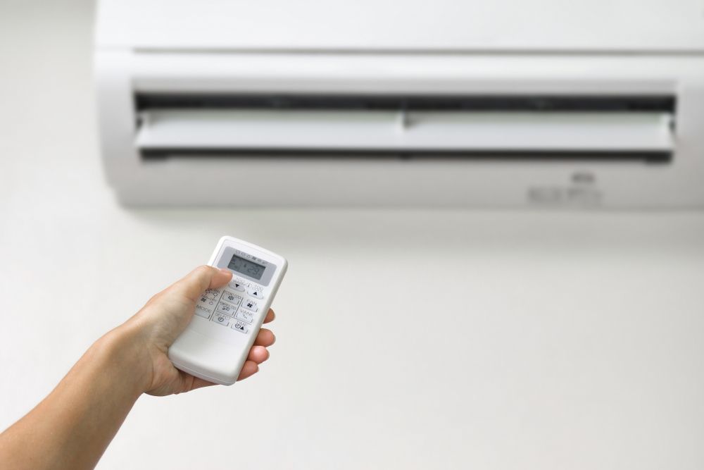 A Person Is Holding A Remote Control In Front Of An Air Conditioner — Law Air Conditioning In Charters Towers, QLD