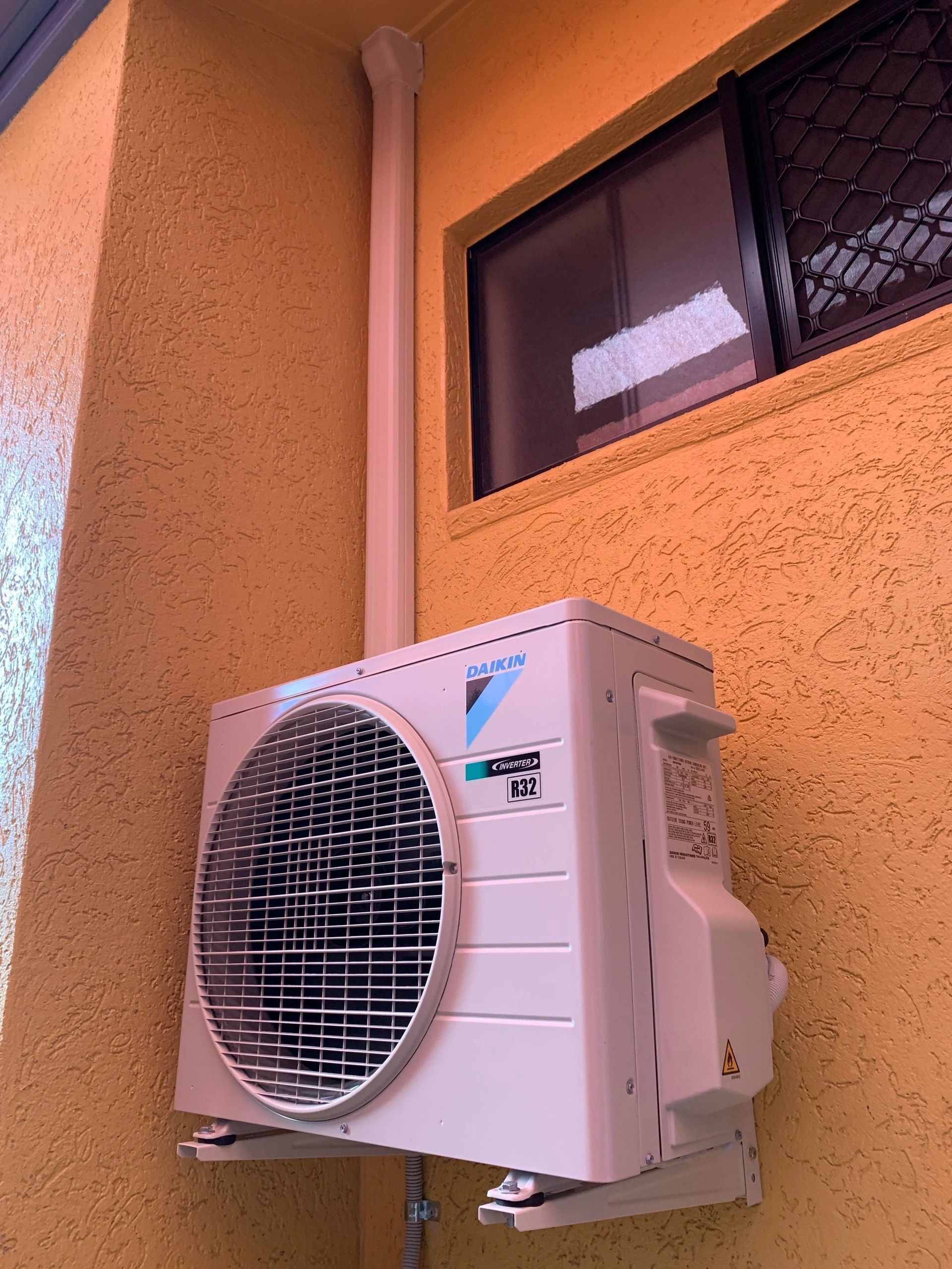 A White Air Conditioner Is Mounted On A Yellow Wall Next To A Window — Law Air Conditioning In Ingham, QLD