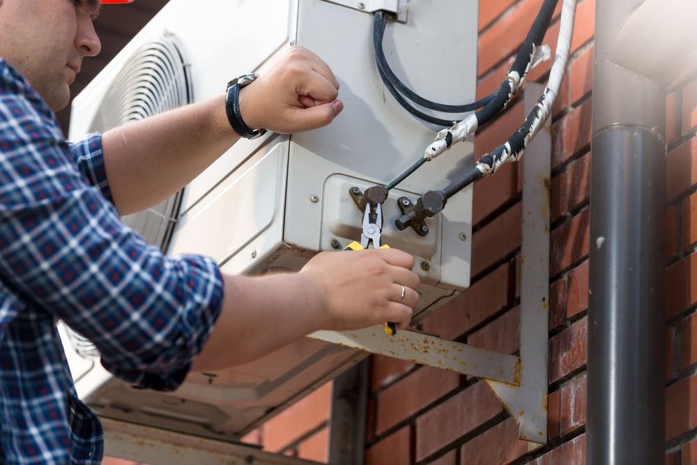 A Man Is Fixing An Air Conditioner On A Brick Wall — Law Air Conditioning In Annandale, QLD