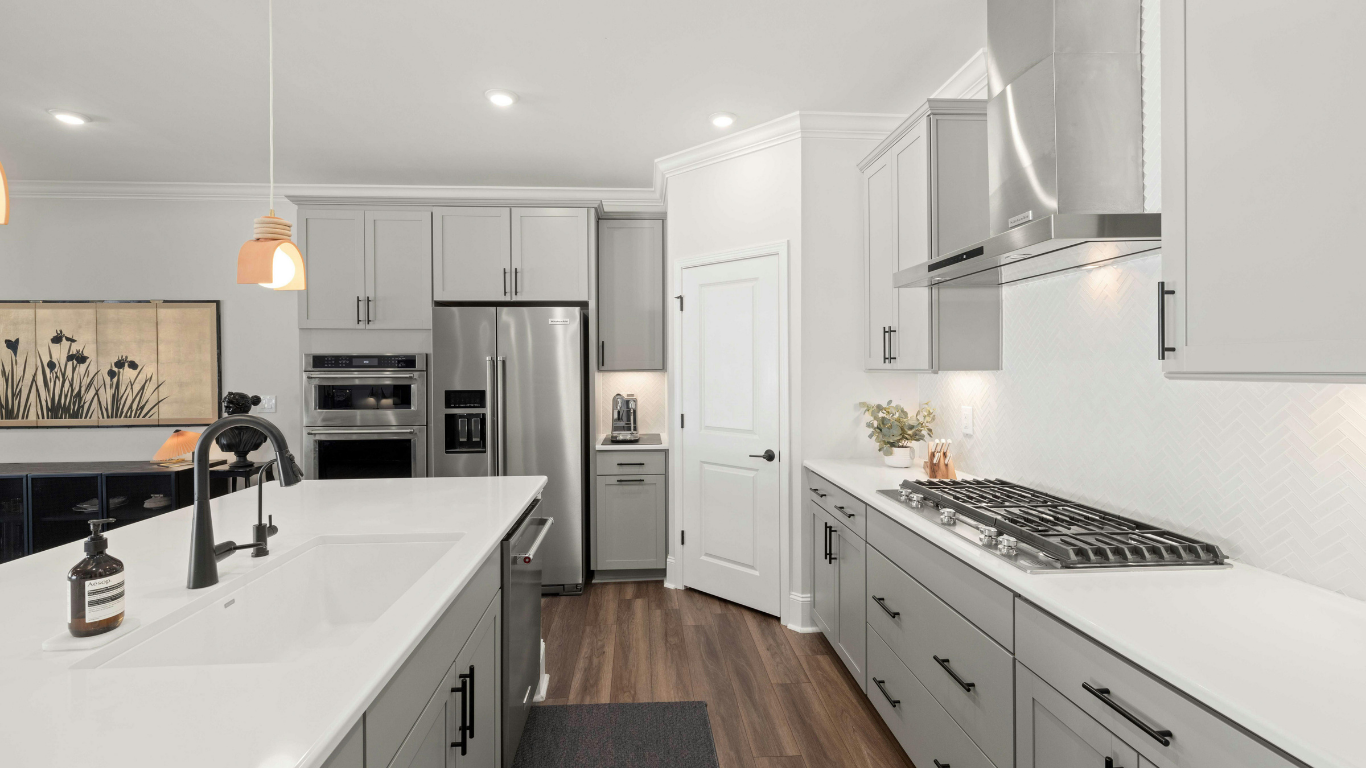 Modern kitchen with white cabinets, stainless steel appliances, and a black-framed window overlooking a backyard.