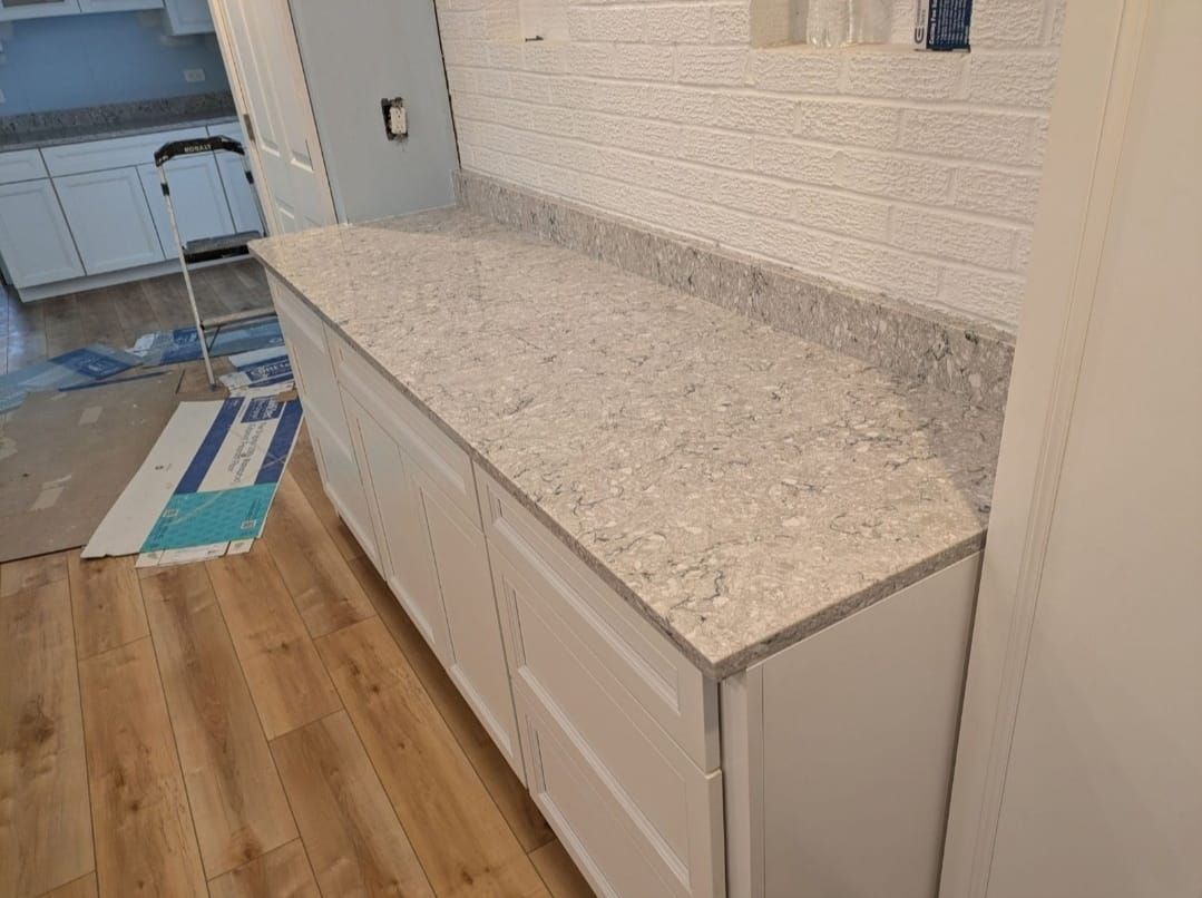 Kitchen counter with speckled stone top, white cabinets, and light wood flooring in a room under renovation