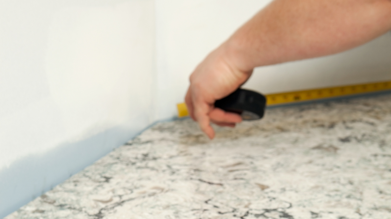 White kitchen with island, marble countertops, cabinets, and a person working.