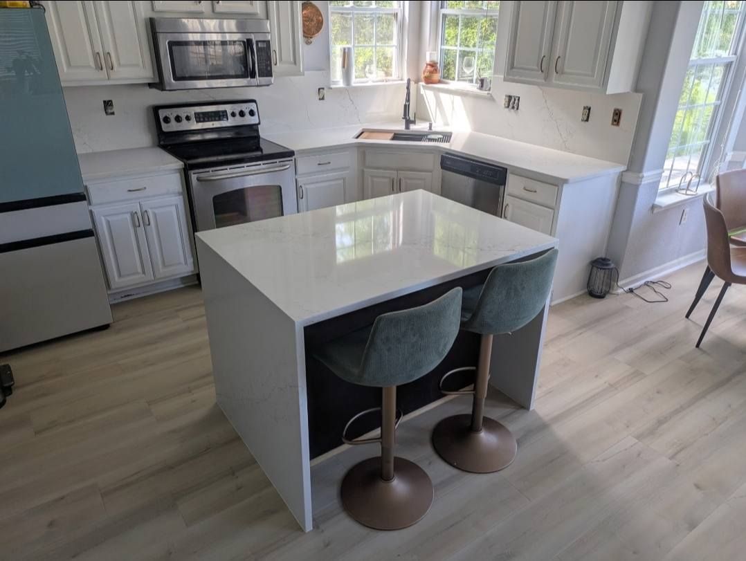 Bright white kitchen with island, black stools, and stainless appliances by large windows