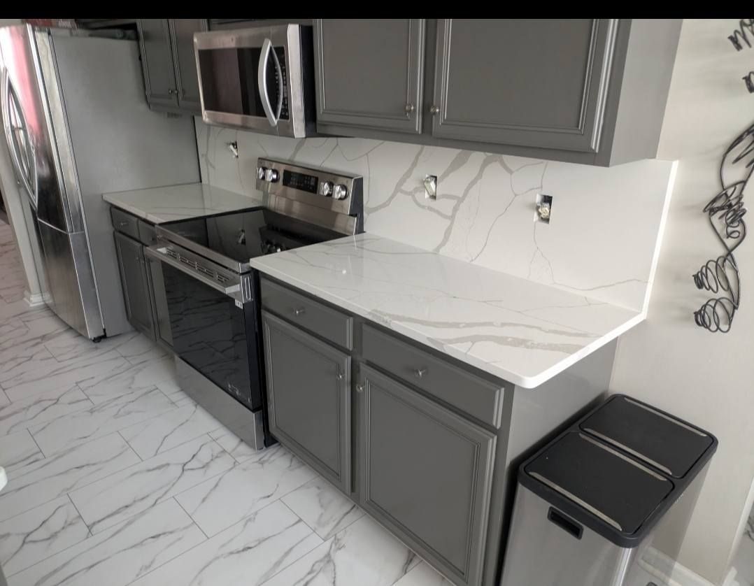 Modern kitchen with gray cabinets, black appliances, white countertops, and a marble-look floor.
