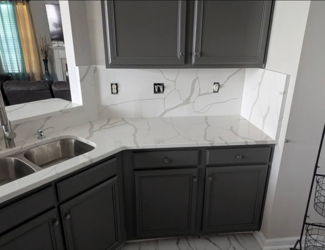 Modern kitchen with dark cabinets, white marble-look backsplash, stainless sink, and countertop appliances removed