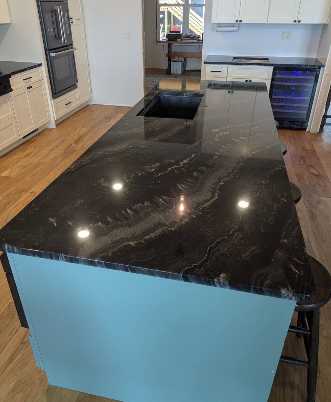 Modern kitchen with black marble island, blue base, stainless appliances, and hardwood floors