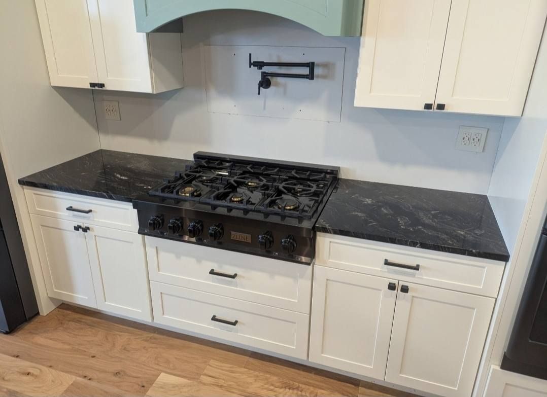 White kitchen with black granite countertop and stainless gas range beneath a blue tile backsplash