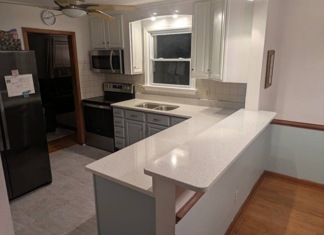 Empty kitchen with white cabinets, black appliances, and a light-colored breakfast bar
