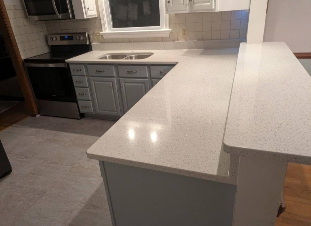 Modern kitchen with white speckled island countertop, gray cabinets, and stainless steel appliances