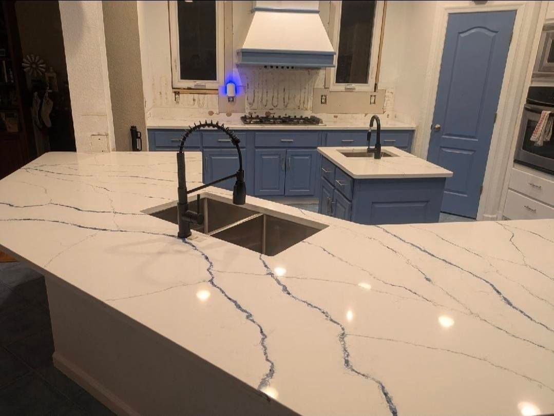 Modern kitchen with white marble island, black faucet, blue cabinets, and blue front door.