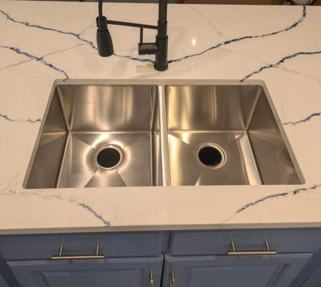Double stainless steel kitchen sink with black faucet and white marble-look countertop.